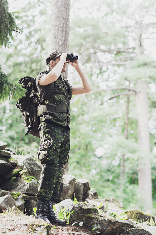hunting, war, army and people concept - young soldier or ranger with binocular and backpack observing forest