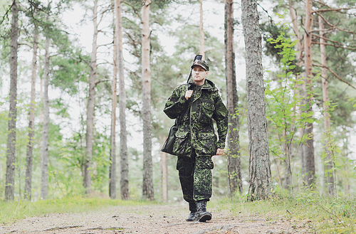hunting, war, army and people concept - young soldier, ranger or hunter with gun walking in forest