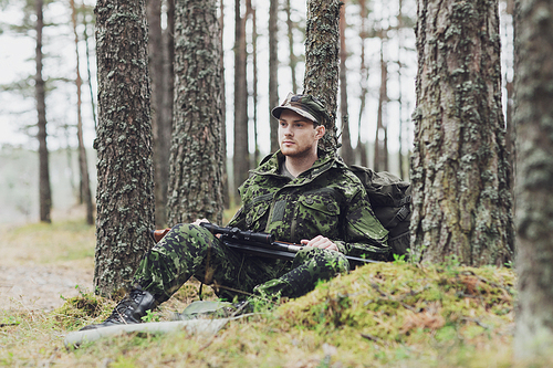 hunting, war, army and people concept - young soldier, ranger or hunter with gun and backpack resting in forest