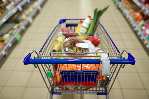consumerism concept - food in shopping cart or trolley at supermarket