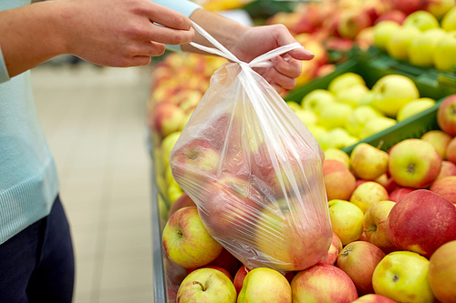 sale, shopping, food, consumerism and people concept - woman tying bag with apples at grocery store