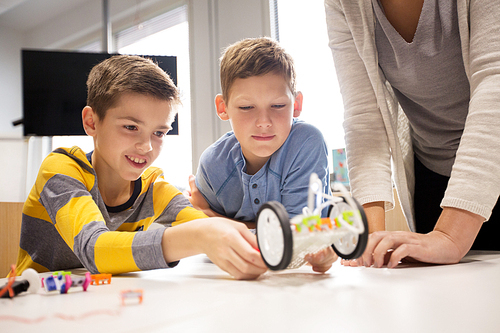 education, children, technology, science and people concept - happy boys and teacher building robot at robotics school lesson