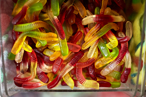 food, junk-food, confectionery and unhealthy eating concept - close up of multicolored gummy worms in transparent plastic box at candy shop