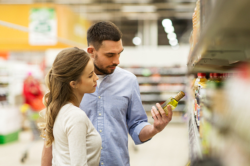 shopping, food, sale, consumerism and people concept - happy couple buying olive oil at grocery store or supermarket