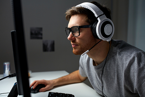 technology, gaming, entertainment, let's play and people concept - young man in headset and glasses with pc computer playing game at home and streaming playthrough or walkthrough video
