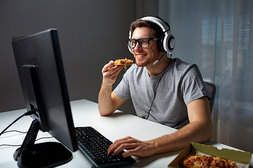 technology, gaming, entertainment, let's play and people concept - happy young man in headset with pc computer eating pizza while playing game at home and streaming playthrough or walkthrough video
