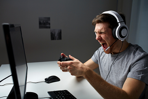 technology, gaming, entertainment, let's play and people concept - angry screaming young man in headset with controller gamepad playing computer game at home and streaming playthrough video