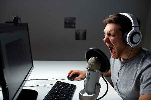 technology, gaming, entertainment, let's play and people concept - angry screaming young man in headset with pc computer playing game at home and streaming playthrough or walkthrough video