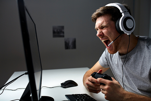 technology, gaming, entertainment, let's play and people concept - screaming young man in headset with controller gamepad playing computer game at home and streaming playthrough or walkthrough video