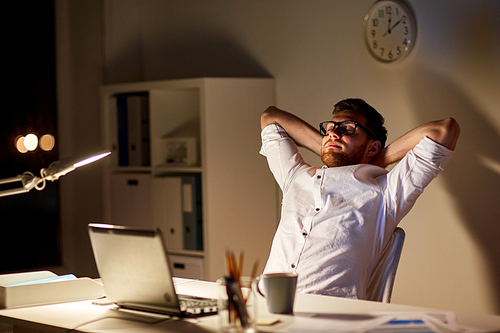 business, overwork, deadline and people concept - tired man with laptop working at night office and stretching