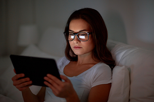 technology, vision, communication and people concept - young woman in glasses with tablet pc computer in bed at home bedroom at night