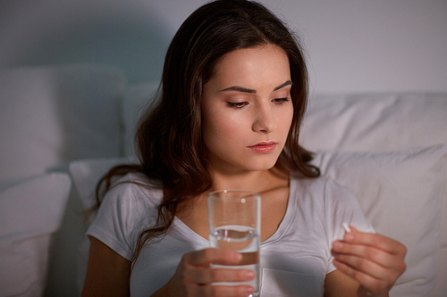 medicine, healthcare and people concept - woman with pill and glass of water in bed at night home
