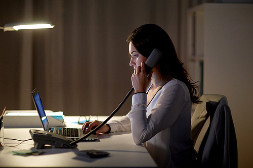 business, overwork, deadline and people concept - woman typing on laptop and calling on phone at night office