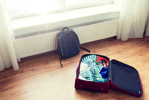 summer vacation, travel, tourism and objects concept - close up of travel bag with beach clothes and backpack on floor at home or hotel room