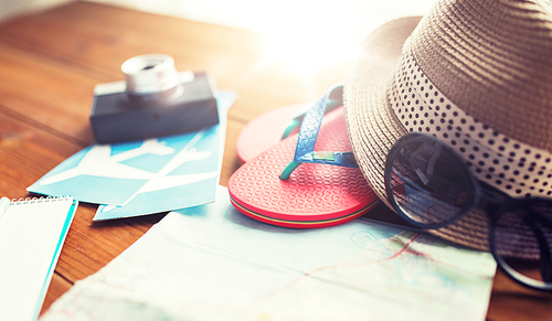 summer vacation, tourism and objects concept - close up of travel map, flip-flops, hat and camera with airplane tickets on wooden table at home