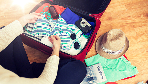 summer vacation, travel, tourism and objects concept - close up of woman packing travel bag for vacation