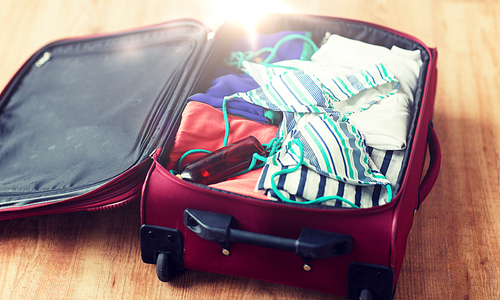 summer vacation, travel, tourism and objects concept - close up of travel bag with beach clothes, sunglasses and sunscreen