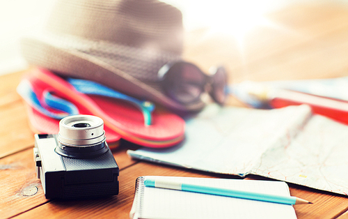summer vacation, travel, tourism and objects concept - close up of camera, notepad with pencil and personal accessories
