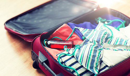 summer vacation, travel, tourism and objects concept - close up of travel bag with beach clothes, sunglasses and sunscreen