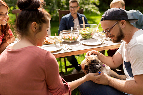 leisure, summer holidays, eating, people and food concept - happy friends with french bulldog dog having dinner at garden party