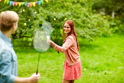leisure, holidays, people and sport concept - happy couple or friends playing badminton or shuttlecock at summer garden