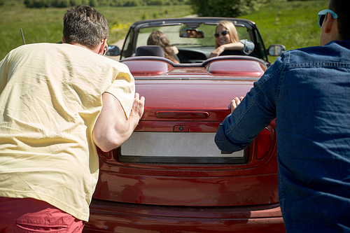 leisure, road trip, travel and people concept - happy friends pushing broken cabriolet car
