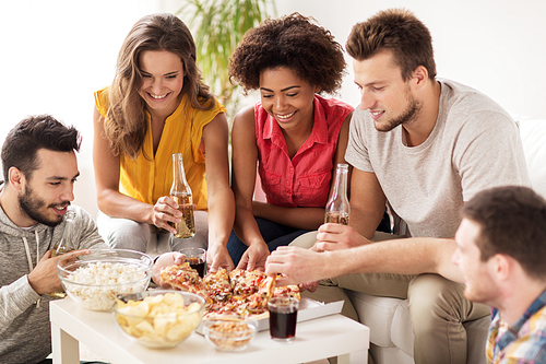 friendship, holidays, fast food and celebration concept - happy friends with drinks and snacks eating pizza at home