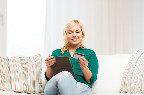 people, internet bank, online shopping, technology and e-money concept - happy young woman sitting on sofa with tablet pc computer and credit card at home