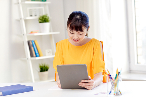 people, education, high school and learning concept - happy asian young woman student with tablet pc computer, book and notepad writing at home