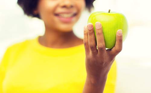 people, food, healthy eating and dental care concept - close up of happy african american young woman with green apple at home