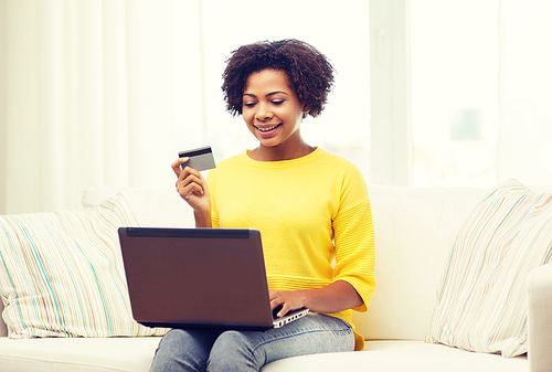 people, internet bank, online shopping, technology and e-money concept - happy african american young woman sitting on sofa with laptop computer and credit card at home