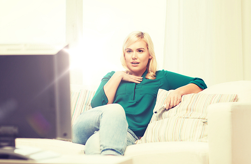 television, leisure and people concept - smiling woman sitting on couch with remote control and watching tv at home