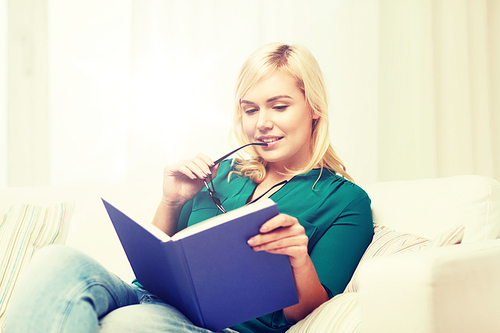 leisure, literature, education and people concept - young woman with glasses reading book at home