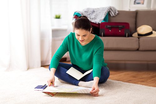 vacation, tourism, travel and people concept - happy young woman with map, notebook and passport at home going on trip