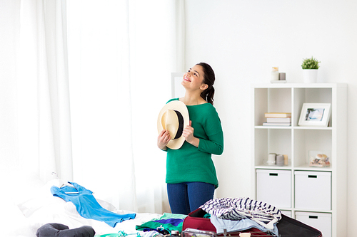 tourism, people and luggage concept - happy young woman with hat packing travel bag at home