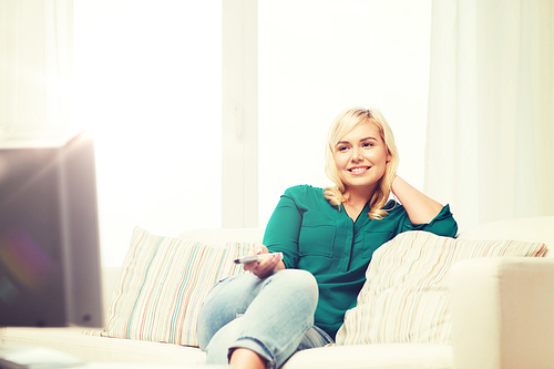 television, leisure and people concept - smiling woman sitting on couch with remote control and watching tv at home