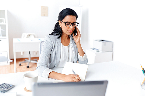 business, technology, communication and people concept - businesswoman or secretary calling on smartphone and writing to notebook at office