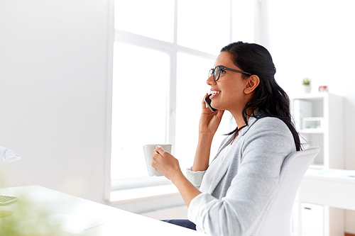 business, communication and people concept - happy businesswoman or secretary calling on smartphone and drinking coffee at office