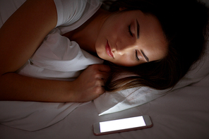 technology and people concept - young woman with smartphone sleeping in bed at home at night