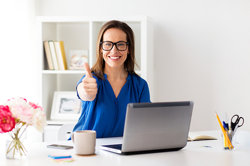 business, people and technology concept - happy smiling woman in glasses with laptop computer showing thumbs up at office