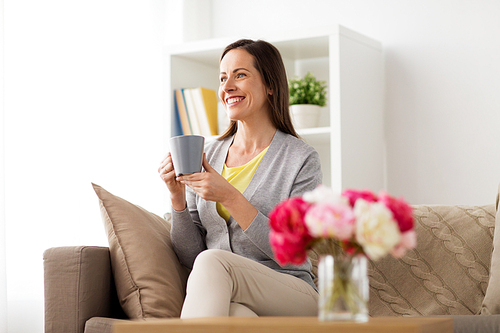 people, drinks and leisure concept - happy woman with mug drinking tea or coffee at home