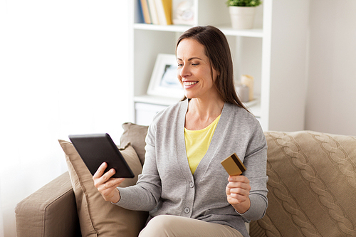 people, technology and shopping online concept - happy woman sitting on sofa with tablet pc computer and bank card at home