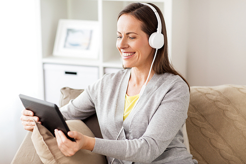 people, technology and leisure concept - happy woman sitting on sofa with tablet pc computer and headphones listening to music at home