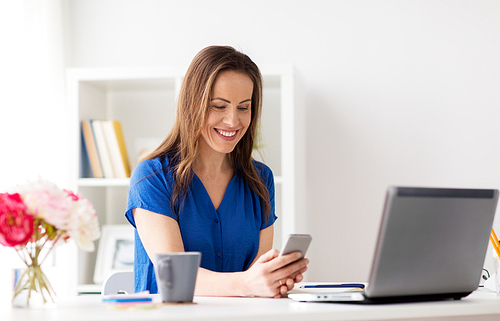 technology, communication and people concept - happy woman with smartphone and laptop computer at office