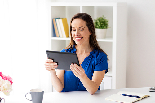 business, people and technology concept - happy smiling woman in glasses with tablet pc computer working at home or office