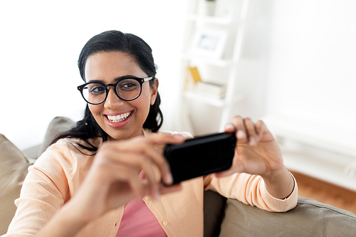 people, technology and leisure concept - happy young indian woman taking selfie on smartphone at home