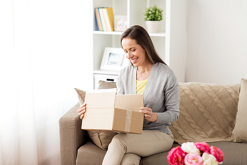 delivery,  and people concept - smiling woman opening cardboard box at home