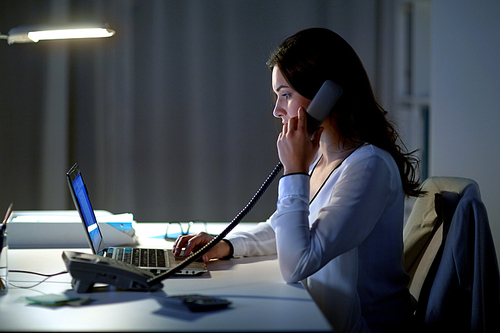 business, overwork, deadline and people concept - woman typing on laptop and calling on phone at night office