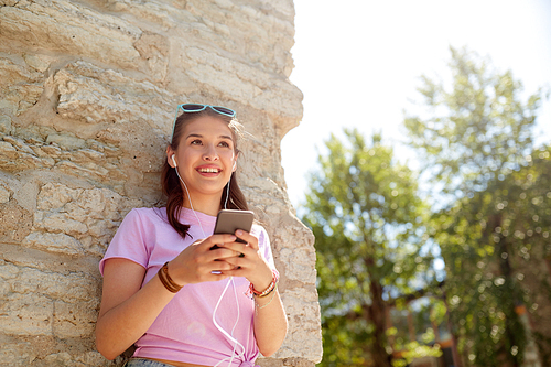 technology, lifestyle and people concept - smiling young woman or teenage girl with smartphone and earphones listening to music outdoors