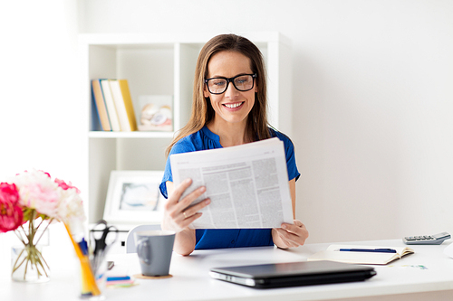 business, people and mass media concept - happy smiling woman in glasses reading newspaper at office